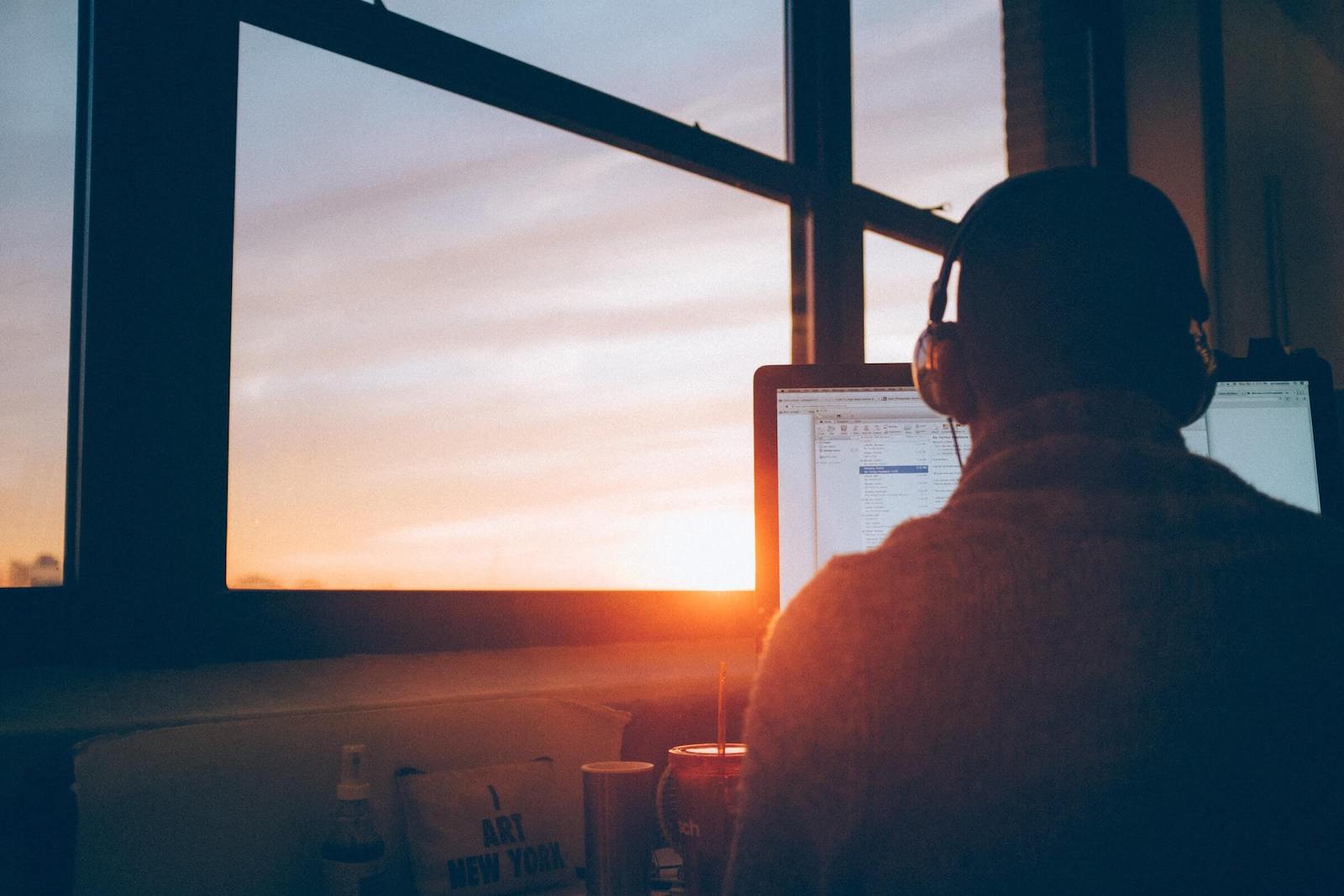 Person with headphones on using a computer looking at a sunset